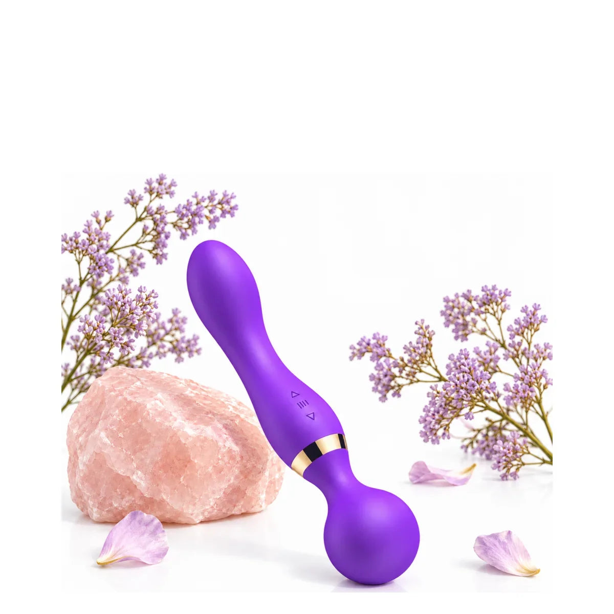 Violetter Vibrator mit goldfarbenem Zierring neben einem rosafarbenen Stein und violetten Blüten.
