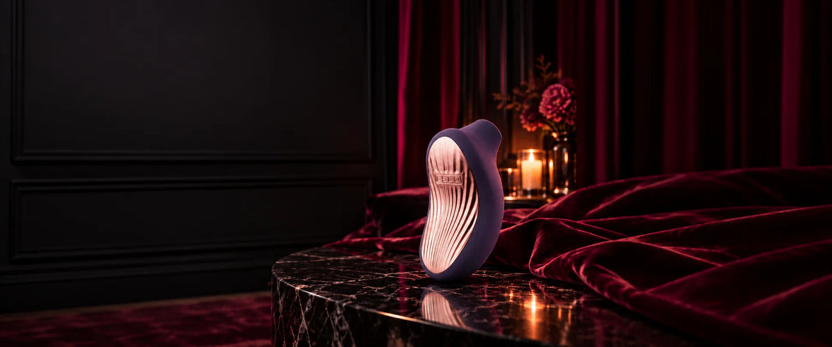 Violetter LELO-Stimulator mit roségoldfarbener Oberfläche auf schwarzem Marmor im warmen Kerzenlicht.