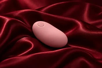 Rosafarbener, ovaler Vibrator auf weinrotem Satin.